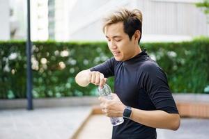 Active Asian sportsman relaxing and drinking a water in bottle after outdoor running or workout. Asian man drink a water during the break from exercise. A healthy man trying hard for cardio workout.