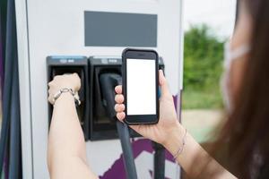 Empty screen of mockup smartphone isolated with clipping path. Asian young woman using ev charging application on smartphone connect with the charging station, BEV or electric vehicle charging station photo