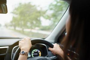 Happy Asian woman driving the electric vehicle - EV car smiling and showing her thumb up to the camera, happy and safety driving concept. Woman driving modern EV car and smiles to camera. photo