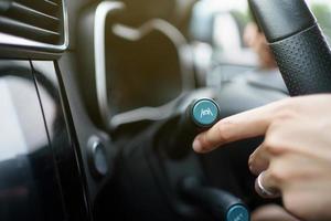 Unrecognizable woman driver activating the adaptive cruise control or steering assistant on the control stick behind steering wheel in electric vehicle - EV car. Driving Assist system in modern car. photo