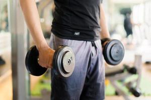 Active Asian sportsman doing a weight exercise in a gym - fitness by lifting up a dumbbell, man sitting on a exercise bench and lift up dumbbells. Sportsman making a shoulder and arms exercise. photo