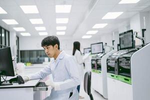 joven científico masculino que busca los resultados del informe del analizador de sangre de automatización en la computadora y una joven científica que trabaja con el analizador de sangre de automatización en el laboratorio médico foto