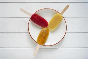 three different fruit smoothie popsicles or ice pops on a plate photo