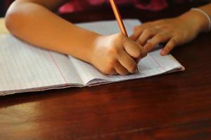 niña escribiendo una lección en un libro con un lápiz foto