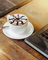 Hot coffee cup and laptop on wood table in the cafe. photo