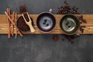 Roasted coffee beans with coffee powder and flavourful ingredients for make tasty coffee setup on dark stone background. photo