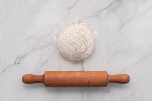 Fresh homemade yeast dough resting on marble table with ears of wheat and rolling pin. photo