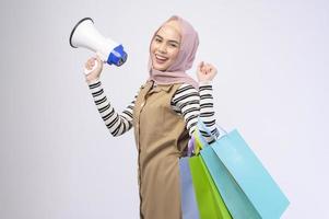 Young beautiful muslim woman in suit holding colorful shopping bags over white background studio photo