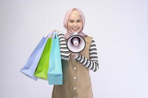 Young beautiful muslim woman in suit holding colorful shopping bags over white background studio photo