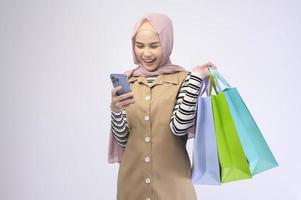 Young beautiful muslim woman in suit holding colorful shopping bags over white background studio photo