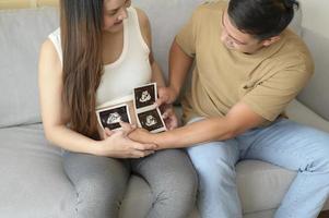 Young pregnant woman with husband holding ultrasound photo of newborn baby, maternity and family concept