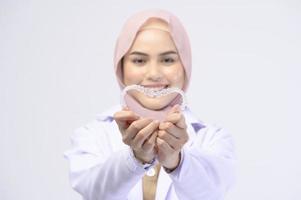 dentista musulmana sosteniendo llaves invisalign sobre estudio de fondo blanco, cuidado de la salud dental y concepto de ortodoncia. foto