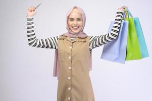 Young beautiful muslim woman in suit holding colorful shopping bags over white background studio photo