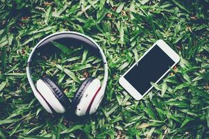 las manos y los auriculares se colocan uno al lado del otro en hierba verde y música cambiante. conceptos de comunicación y escucha. foto