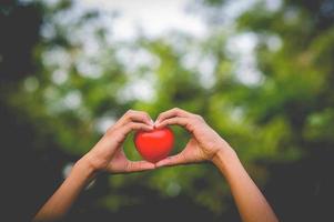 la mano del niño sostiene una hermosa forma de corazón rojo en el fondo natural. amor y san valentin st. enamorado foto