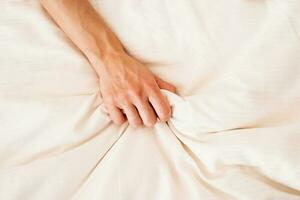 Female hand grasping on white bed, sign of woman orgasm photo