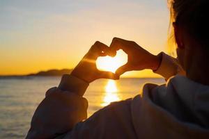 forma de corazón con manos femeninas sobre el fondo del cielo al atardecer foto