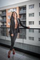 Gorgeous glamour brunette woman with black jacket posing on modern balcony with amazing view on city .Portrait of a Stylish fashionable woman with long legs , black jeans wearing in balcony photo