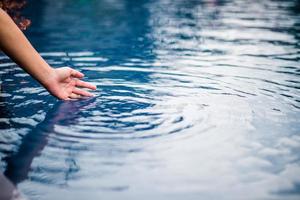 The hand that touches the blue water. The pool is clean and bright. With a drop of water on the water. photo