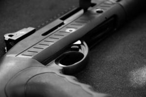 Closeup view of black shotgun which is on the black leather background, concept for shooting sport, security and bodyguard training, soft and selective focus. photo