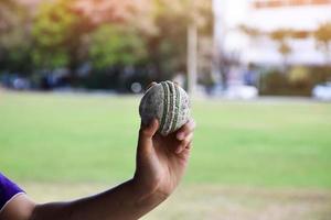 Cricket ball for practising or training hoiding in hand, blurred green grass court background, concept for cricket sport lovers around the world. photo