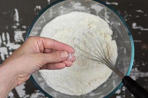 Pinch sea salt on woman hand before putting into flour on brown background photo