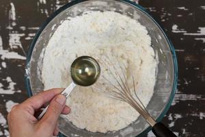 Table spoon with oil in woman hand before putting into flour on brown background photo