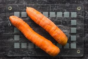 Top view of two unpeeled carrots on glass cutboard before peeling on the black background photo