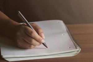 A man writing with a pen in Notebook diary In the concept of business office and education , there is sunlight coming in, Close up. photo