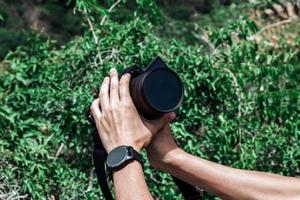 cerca de la mano y la cámara, fotógrafo profesional con una cámara a punto de fotografiar la naturaleza en medio de la selva tropical, ideas de viaje y ocio. foto