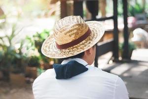 viajero masculino con sombrero de paja, camisa blanca, relajándose en un café natural, vista desde atrás. foto