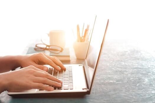 Close up shot of male hands typing on laptop while sitting at office desk indoors, man fingers tapping and texting on computer keyboard while working in cabinet, Work concept. photo