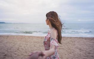 pareja de luna de miel tomándose de la mano y sígueme en la playa