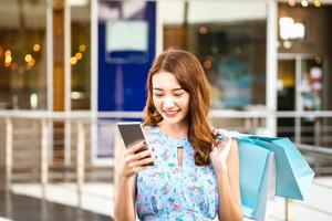una joven compradora asiática usa un teléfono inteligente con bolsas de compras foto