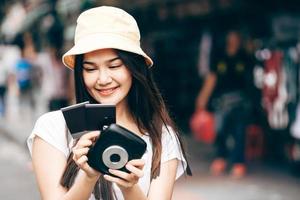 adulto joven viajero asiático feliz mujer sosteniendo cámara instantánea película foto