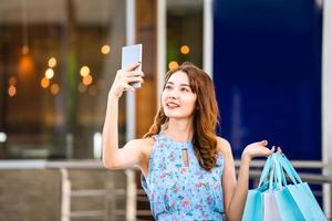 una joven compradora asiática usa un teléfono inteligente con bolsas de compras