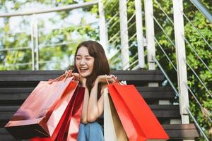 mujer asiática joven sonrisa disfruta de compras con bolsa roja foto