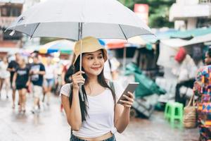 joven mujer adulta de asia con paraguas usa un teléfono inteligente para viajar en bangkok. foto