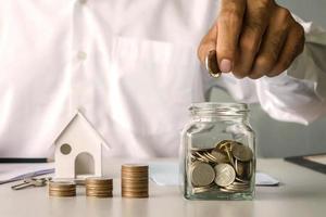 Businessman putting money in a savings bottle and house model, financial concept. Home Mortgage and Residential Real Estate Loans photo