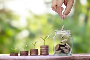 Hand holding silver coins in a jar for saving money and plants growing on piles of money concept coins. Savings and investments grow high. photo