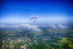 Para-motor flies high above vast fields and village with blue sky on background. photo