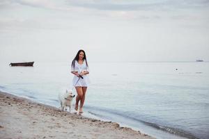 Beautiful brunette woman on the beach with a dog walking photo