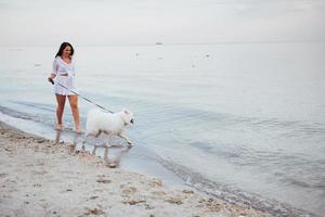 hermosa mujer morena en la playa con un perro caminando foto