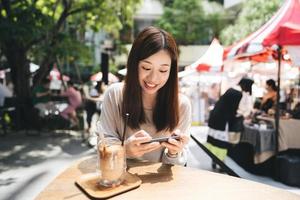 relaje a la mujer asiática en el café usando un teléfono inteligente para las redes sociales. foto