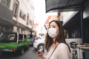 mujer soltera asiática joven de negocios usa máscara para el virus corona o covid19 en la ciudad al aire libre foto