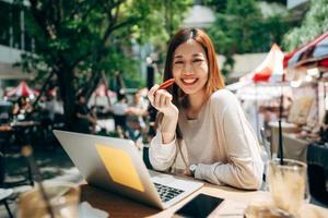 Mujer asiática adulta independiente de negocios que usa una computadora portátil para trabajar en un café en la acera