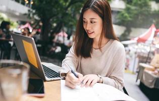 Mujer asiática adulta independiente de negocios que usa una computadora portátil para trabajar en un café en la acera foto