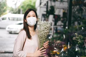 mujer asiática adulta usa mascarilla comprando flores en el quiosco el día. foto