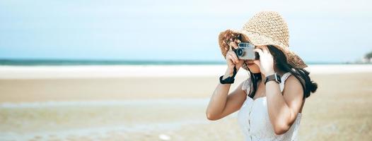 joven mujer asiática adulta cámara de película vintage relajarse viajar en la playa del mar el día. foto