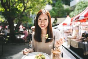 una joven asiática adulta almuerza en un restaurante al aire libre el día del fin de semana